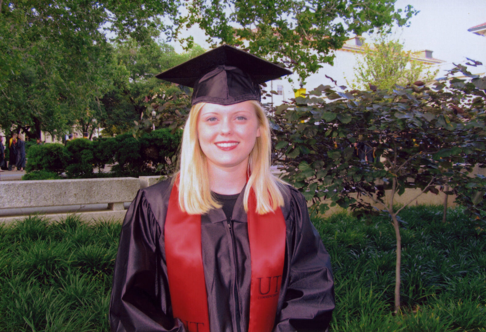 Young woman in graduation gown and cap smiling outdoors.
