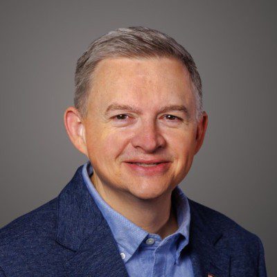 Professional headshot of a middle-aged man in a blue suit and light blue shirt.