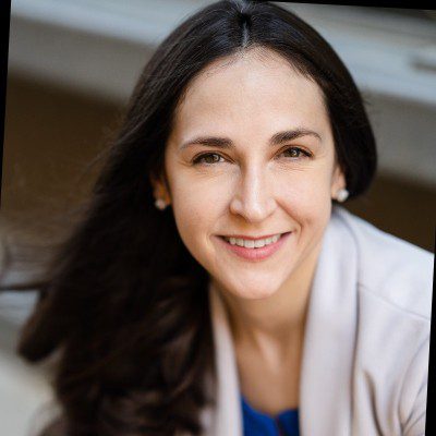 Smiling woman with long dark hair wearing a white jacket.