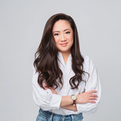 Confident young woman with long wavy hair smiles with arms crossed.