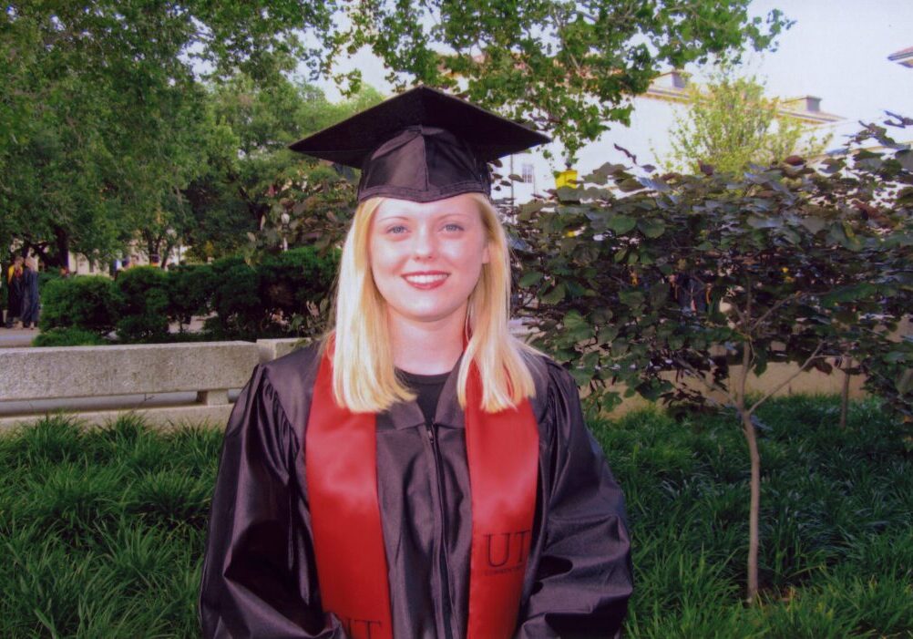 Young woman in graduation gown and cap smiling outdoors.