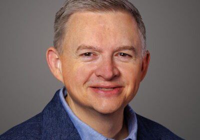 Professional headshot of a middle-aged man in a blue suit and light blue shirt.